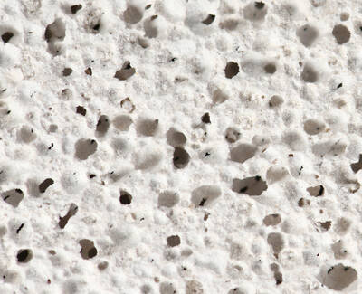 Close-up of a textured surface resembling porous white material, featuring numerous small holes and variations in texture.