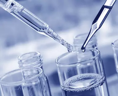 Close-up of two pipettes above a glass container, with droplets of liquid poised to be released into a transparent solution. The image has a cool blue tint.
