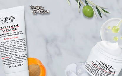 Product display featuring Kiehl's Ultra Facial Cleanser, Toner, and Cream on a marble background, along with citrus fruits and skincare accessories.