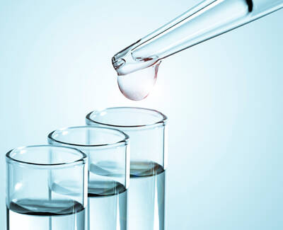 A dropper releasing a drop of liquid above three glass test tubes filled with different colored liquids.