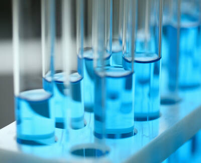 A close-up of several test tubes filled with a blue liquid, arranged in a test tube rack. The background is softly blurred, highlighting the vibrant blue colors of the liquids.