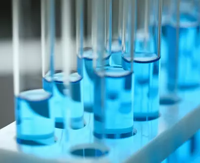 A close-up of several test tubes filled with a blue liquid, arranged in a test tube rack. The background is softly blurred, highlighting the vibrant blue colors of the liquids.