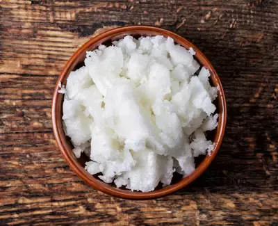 A small bowl filled with white, fluffy texture resembling snow or finely grated coconut, placed on a rustic wooden surface.