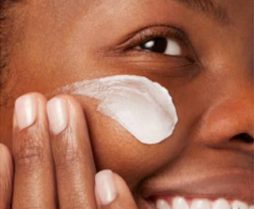 A woman applies an overnight hydrating mask to her cheek.