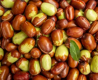 A close-up view of a pile of jujube fruits, featuring a mix of red and green varieties, with a fresh green leaf among them.
