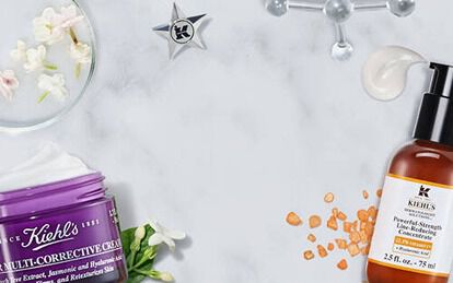 A flat lay of Kiehl's skincare products, including a serum and a cream, arranged on a marble surface alongside floral and natural elements.