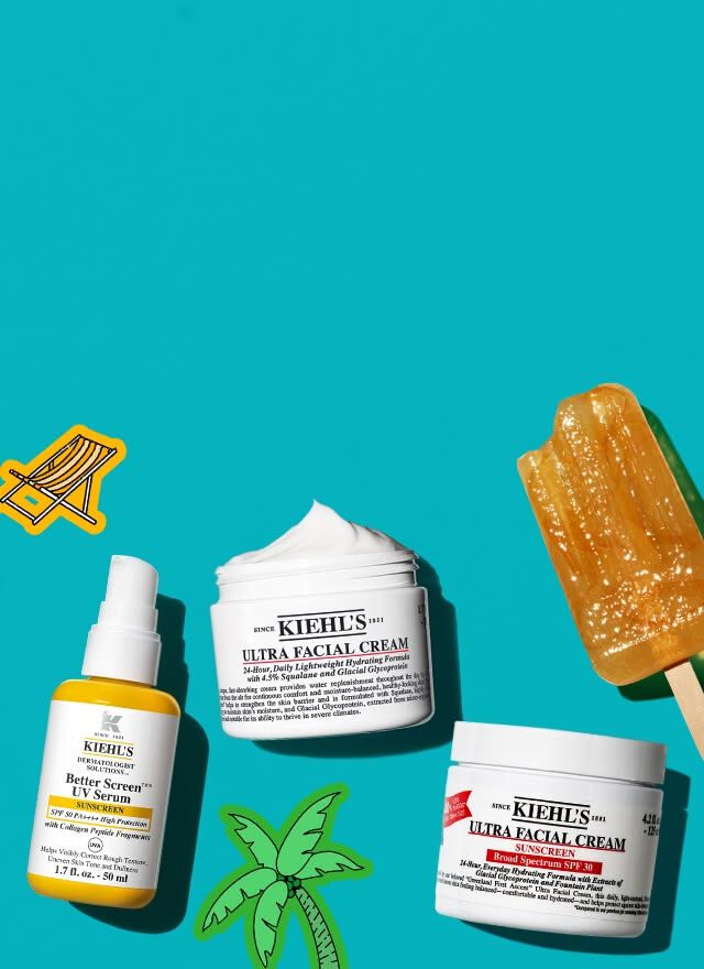 Flat lay of Kiehl's skincare products including UV serum, Ultra Facial Cream, and sunscreen jar with an orange popsicle on a purple-striped cloth background.