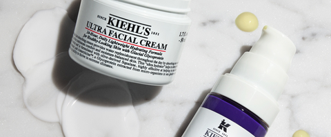 A close-up of a bottle of Kiehl's Retinol Skin-Renewing Daily Micro-Dose Serum, placed on a marble surface with a small amount of white cream next to it.