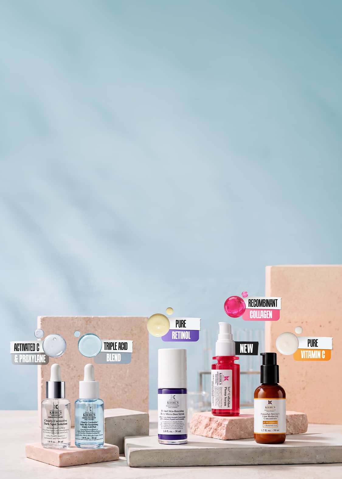 Kiehl's skincare product lineup on stone podiums, featuring five serums with ingredient labels for Activated C & Proxylane, Triple Acid Blend, Pure Retinol, Recombinant Collagen, and Pure Vitamin C.​