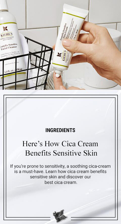 A clean bathroom setting featuring Kiehl's Cica Cream and a gentle facial cleanser. A hand holds the Cica Cream tube, and a wire basket displays the cleanser, emphasizing skincare for sensitive skin.