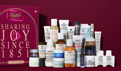 Kiehl’s Advent Calendar gift box in deep red with gold text, displayed next to 24 mini skincare products including Ultra Facial Cream, Calendula Toner, Retinol Serum, and Lip Balm #1. A pink spray-paint graphic on the side calls out the value of the set.