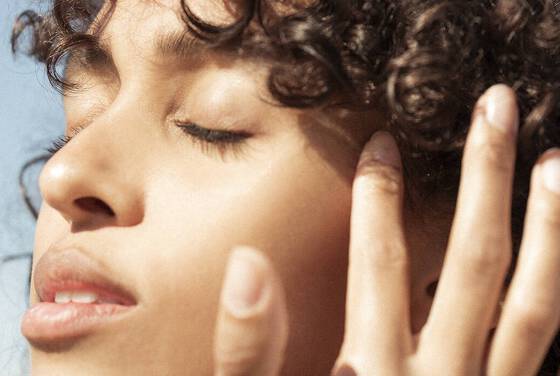 A clos-up shot of a young woman with tanned skin’s face, glowing in the sun.