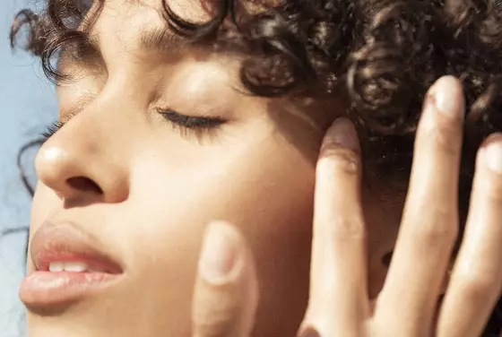 A clos-up shot of a young woman with tanned skin’s face, glowing in the sun.