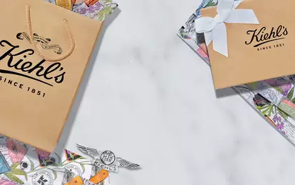 A collection of Kiehl's gift bags and parcels arranged on a marble surface, featuring colorful wrapping paper and a vintage photo of Kiehl's staff.