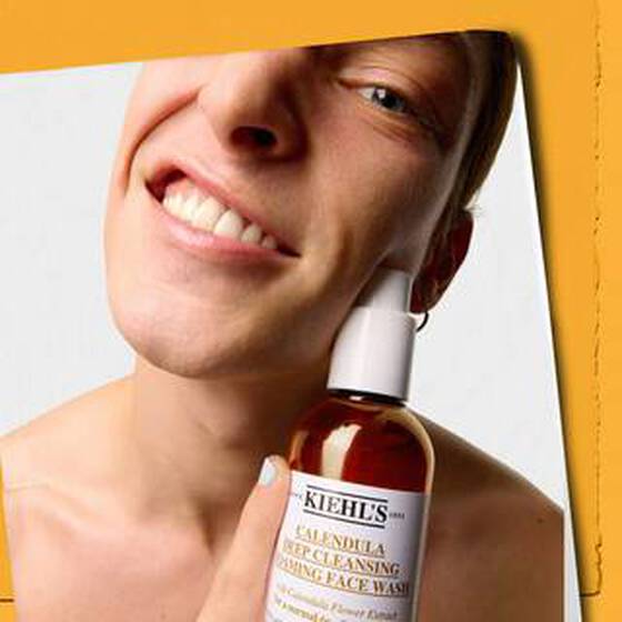 A man holds a bottle of Kiehl’s Calendula Deep Cleansing Foaming Face Wash up to their face.